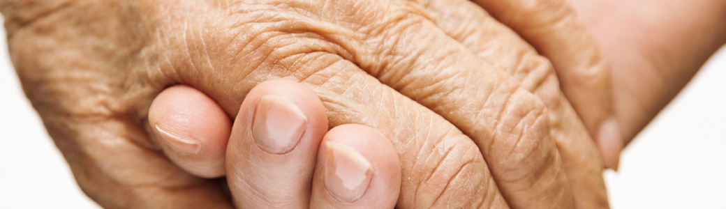 Adult hand holding a limp elderly person's hand